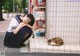 A woman sitting on the sidewalk next to a cat.