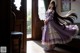 A woman in a purple dress standing in front of a window.